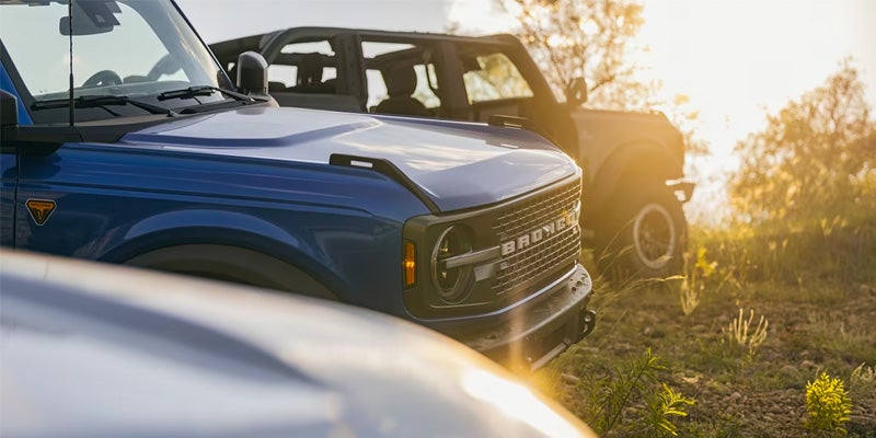 A view of the sun setting and light reflecting off the hoods of two 2024 Ford Broncos parked in the grass