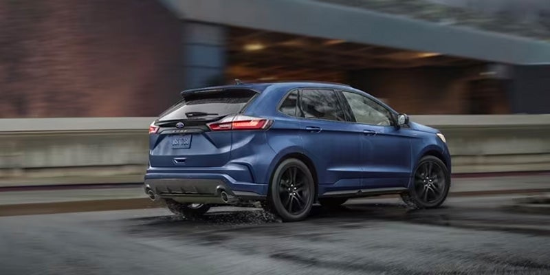 A blue 2024 Ford Edge driving down a city street on a rainy day