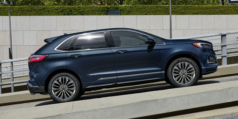passenger side view of a dark blue 2024 Ford Edge driving uphill in a city