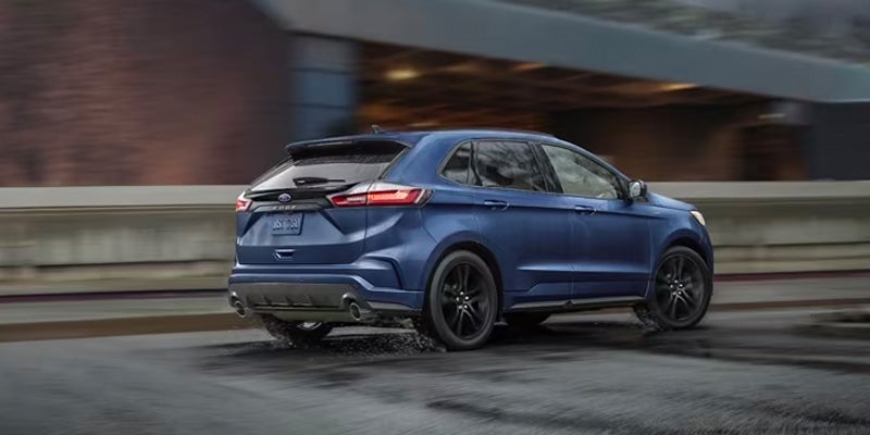 A blue 2024 Ford Edge driving fast through a city at night time