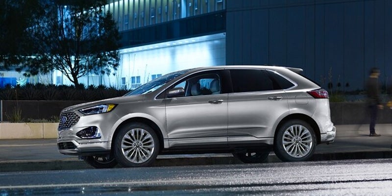 driver side view of a silver 2024 Ford Edge driving down a city street at night