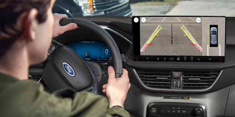 view of a man with both hands on the steering wheel and checking his rear backup camera safety feature displayed on the infotainment system screen in a 2024 Ford Escape