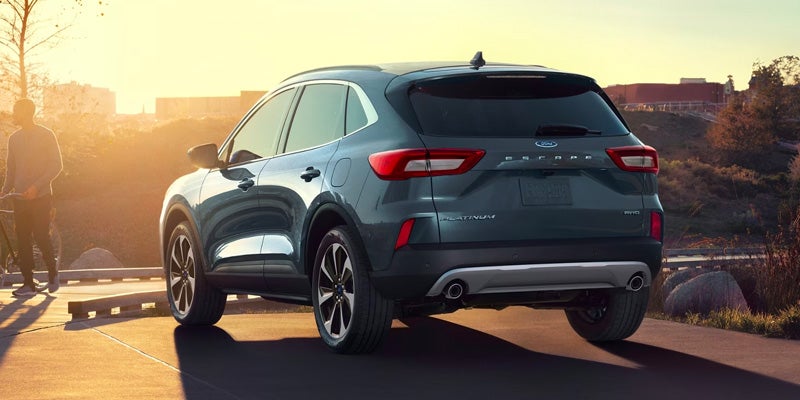 rear view of a silver 2024 Ford Escape parked on the side of a road with the sun setting over a hill in the background