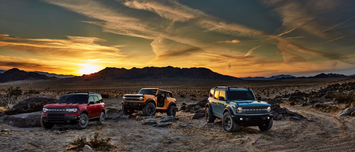 Three 2022 Ford Broncos parked in front of a rocky mountain range at sunset