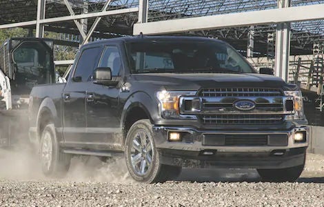 A black Ford F-150 hauling construction equipment a cross a construction site