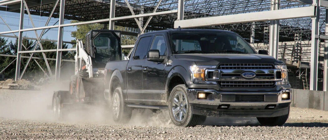 A black 2019 Ford F-150 towing construction equipment